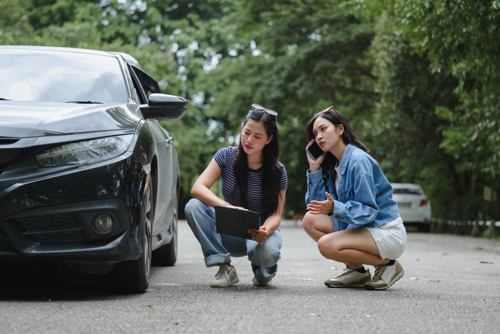two women examining damaged vehicle after a car accident - Is it illegal to settle a car accident privately