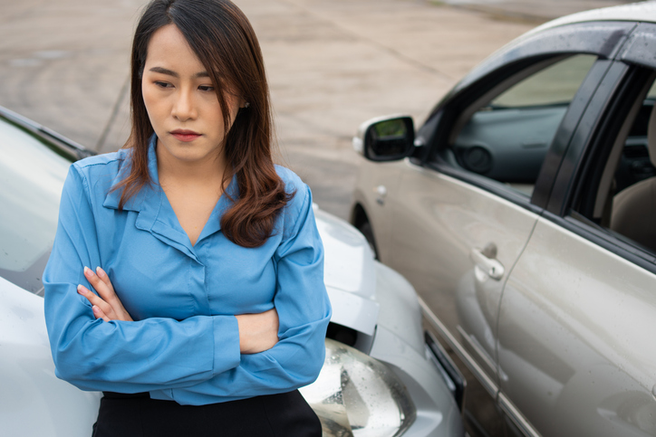 Woman with crossed arms standing next to car accident scene - can you reopen a settled car accident case?
